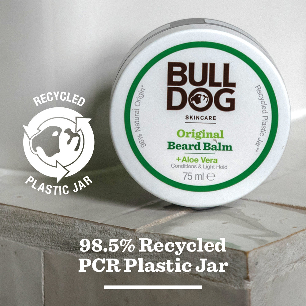 A round jar of Original Beard Balm sits on tiles, featuring a label that notes natural origin ingredients and a jar made from 98.5% recycled PCR plastic. A recycled plastic icon is also visible on the packaging.