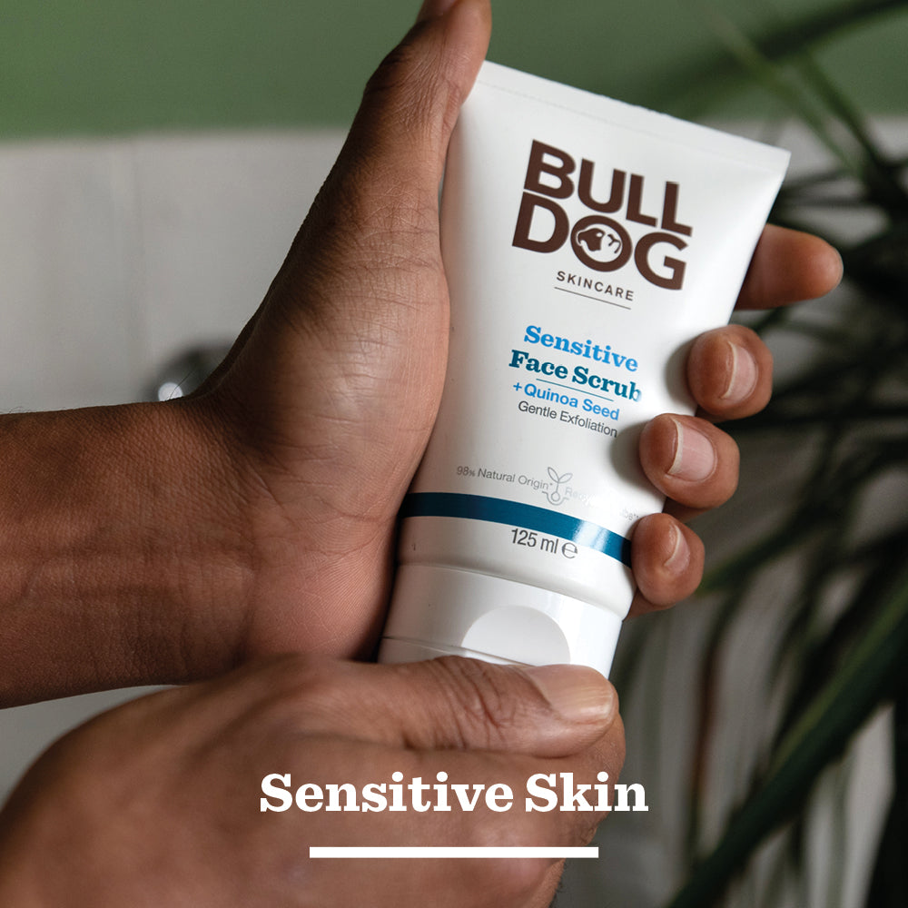 A person holds a tube of Sensitive Face Scrub in their hands, the label clearly visible. Sensitive Skin appears at the bottom, emphasizing its natural origin ingredients.