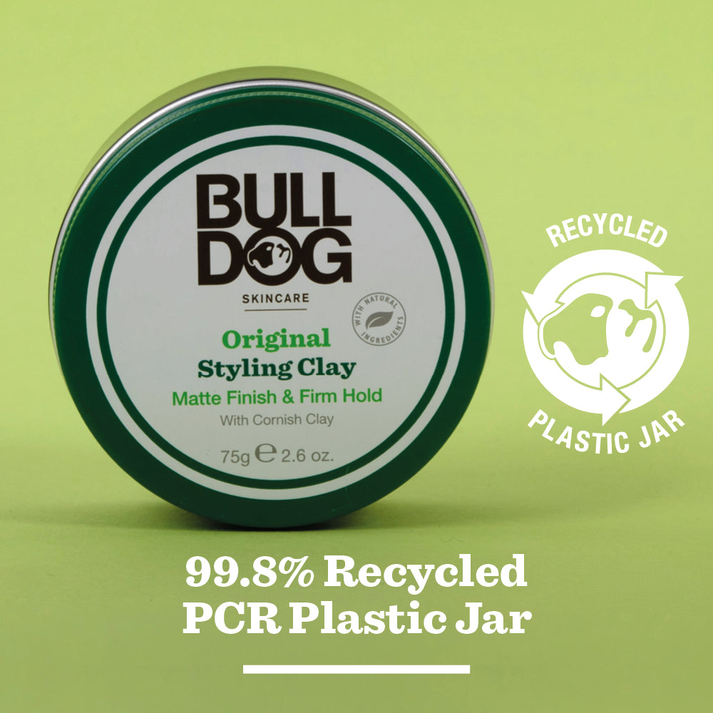 A round tin of Original Hair Styling Clay rests on a green surface; its label highlights a matte finish, firm hold, and notes the 99.8% recycled PCR plastic jar with a recycling logo. Kaolin clay is featured in the formula.